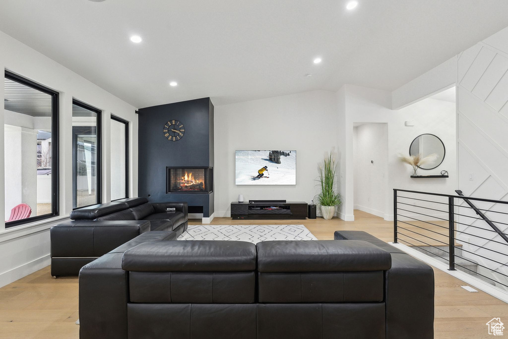 Living area with vaulted ceiling, a large fireplace, light wood finished floors, recessed lighting, and baseboards