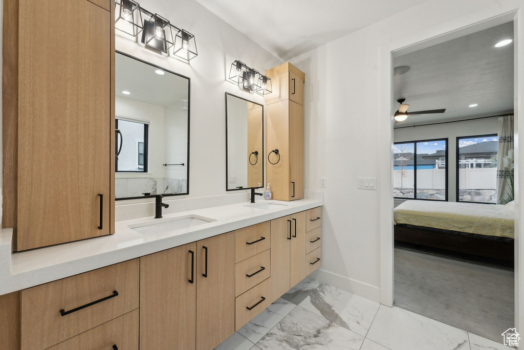 Full bath featuring ensuite bathroom, double vanity, marble finish floors, baseboards, and a ceiling fan