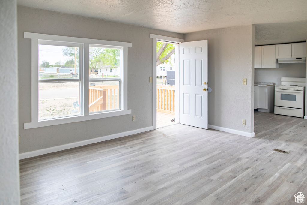 Unfurnished dining area featuring baseboards, light wood-style flooring, and a textured ceiling