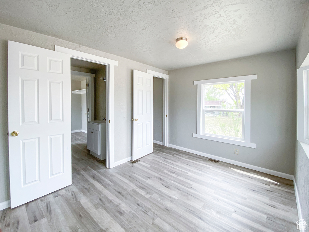 Unfurnished bedroom featuring a textured ceiling, baseboards, and light wood-type flooring