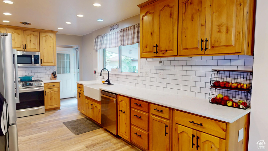Kitchen featuring stainless steel appliances, backsplash, recessed lighting, light wood-type flooring, and light countertops