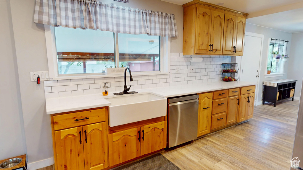 Kitchen featuring stainless steel dishwasher, a sink, light wood finished floors, backsplash, and light countertops