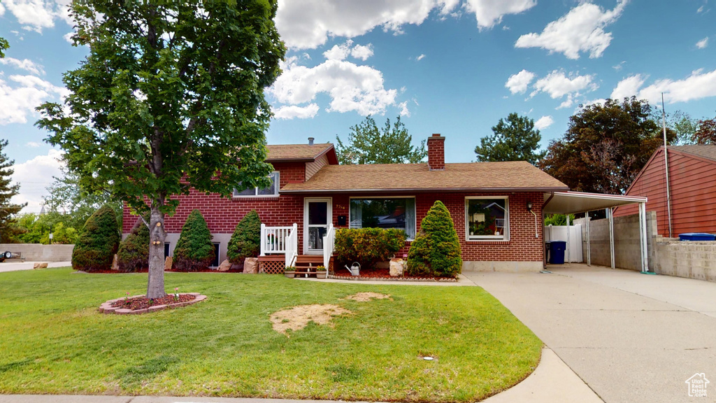 Tri-level home featuring concrete driveway, a chimney, brick siding, a carport, and roof with shingles