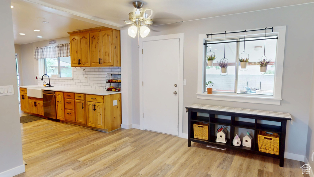 Kitchen with stainless steel dishwasher, light wood-type flooring, a sink, light countertops, and decorative backsplash