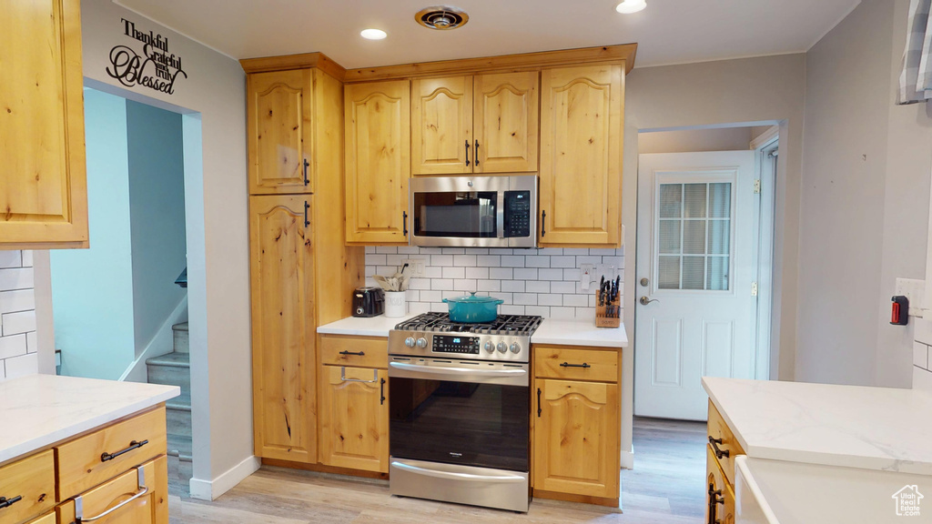 Kitchen with appliances with stainless steel finishes, light wood-style flooring, light brown cabinets, decorative backsplash, and recessed lighting