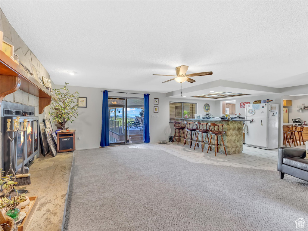 Living room with bar area, ceiling fan, light colored carpet, a textured ceiling, and light tile patterned floors
