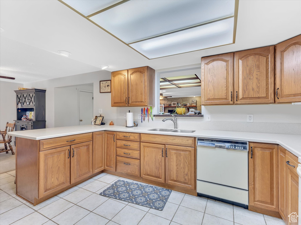 Kitchen featuring white dishwasher, a sink, a peninsula, light countertops, and light tile patterned floors
