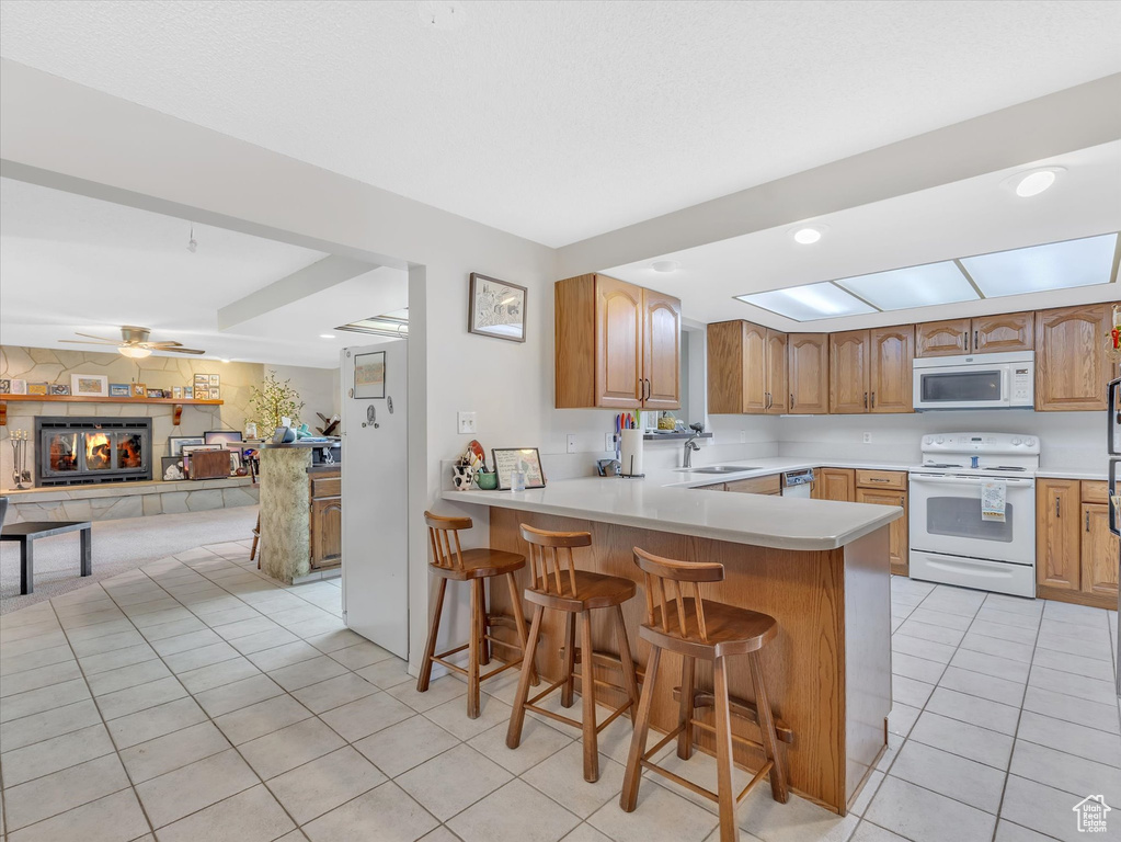 Kitchen featuring white appliances, a sink, light tile patterned floors, a breakfast bar, and a peninsula
