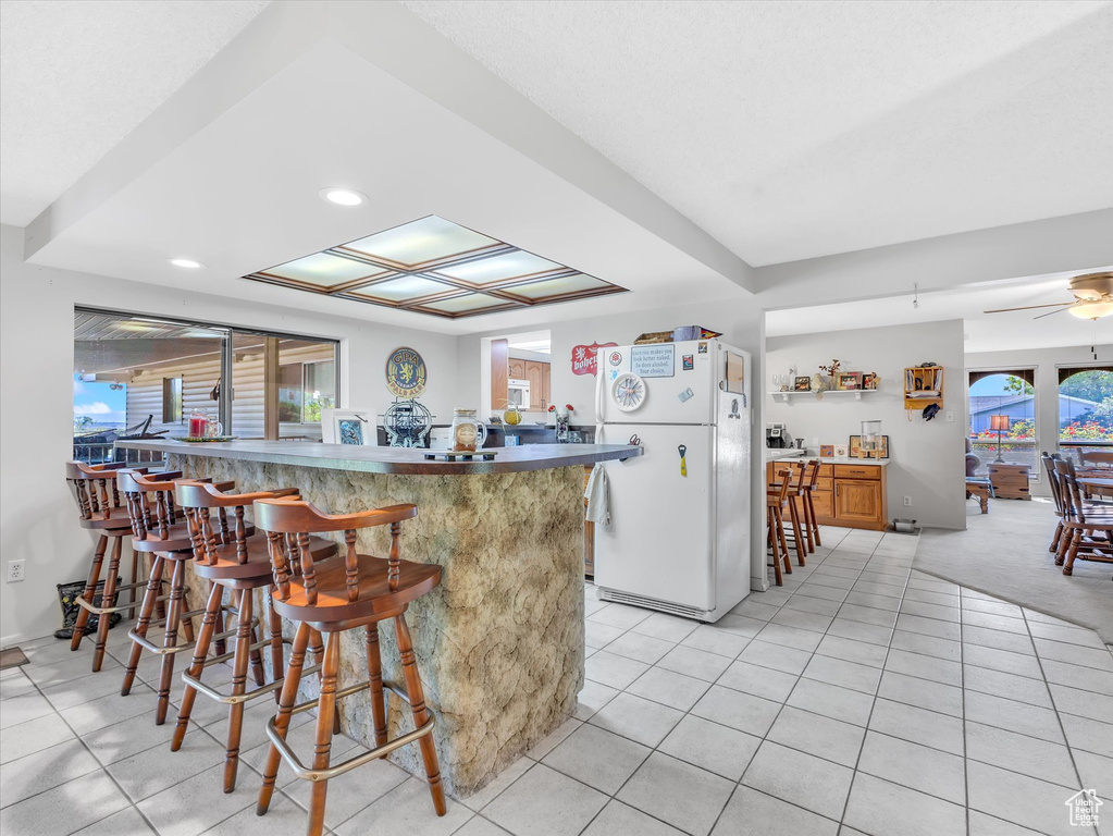 Kitchen featuring freestanding refrigerator, a breakfast bar, light tile patterned floors, a peninsula, and recessed lighting