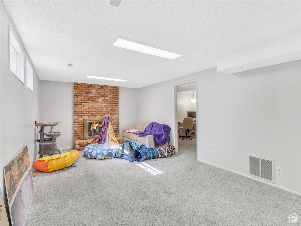 Playroom featuring carpet, a textured ceiling, a brick fireplace, an office area, and baseboards