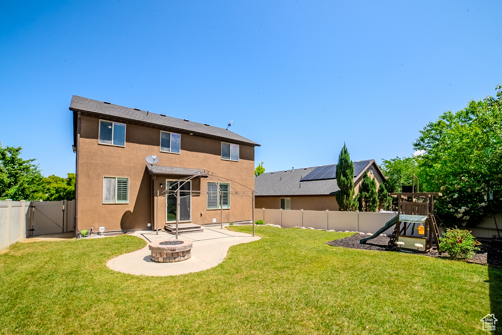 Rear view of house featuring a playground, a gate, stucco siding, a patio, and a fire pit
