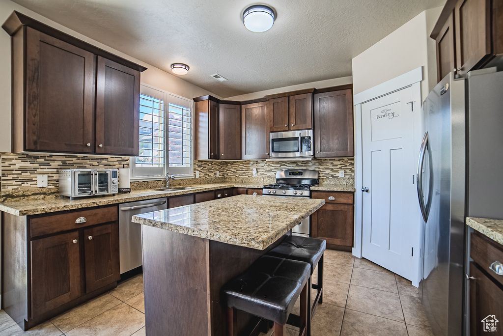 Kitchen featuring appliances with stainless steel finishes, a sink, backsplash, dark brown cabinets, and a textured ceiling