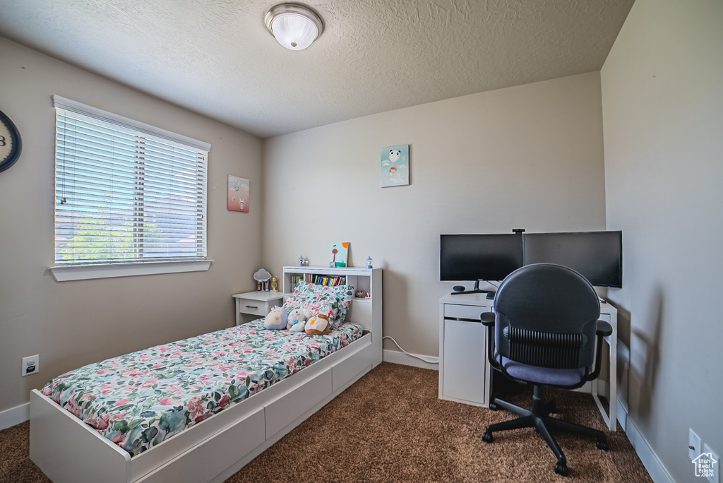 Bedroom featuring dark carpet, a textured ceiling, baseboards, and a desk