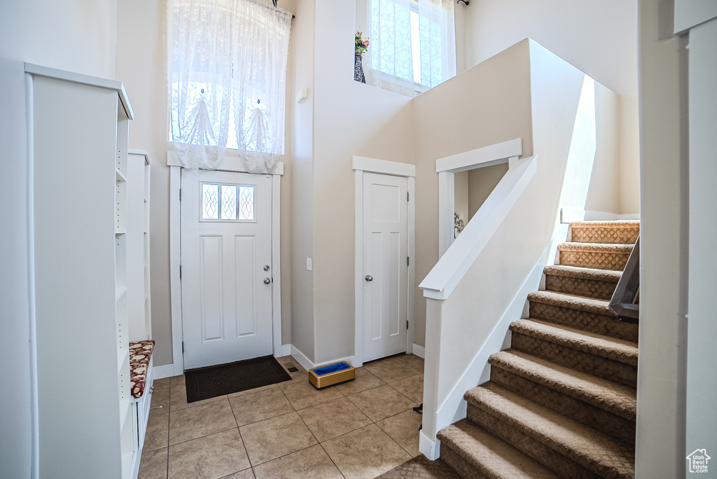 Entryway with a high ceiling, plenty of natural light, stairs, light tile patterned floors, and baseboards