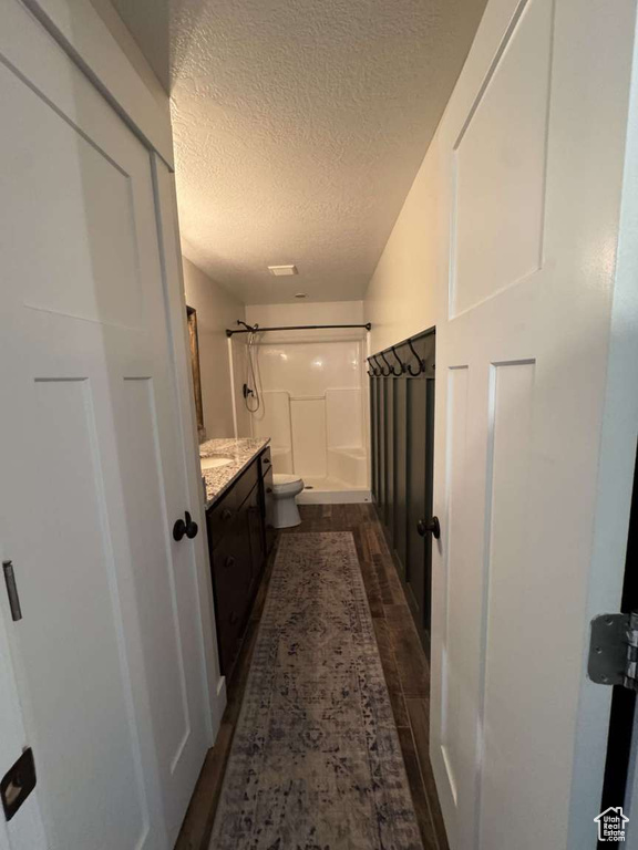 Full bath with a shower, vanity, a textured ceiling, wood finished floors, and toilet