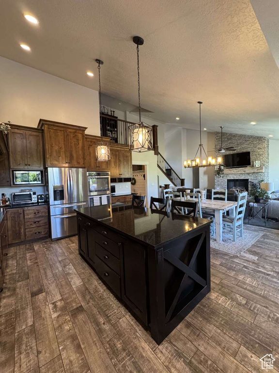 Kitchen featuring appliances with stainless steel finishes, dark wood-style floors, a stone fireplace, a textured ceiling, and a chandelier
