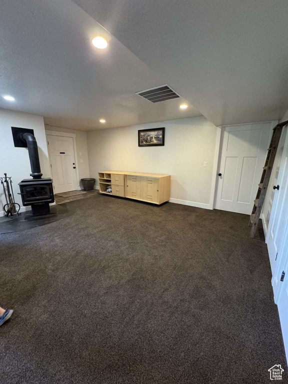 Unfurnished living room with a wood stove, recessed lighting, dark colored carpet, and baseboards