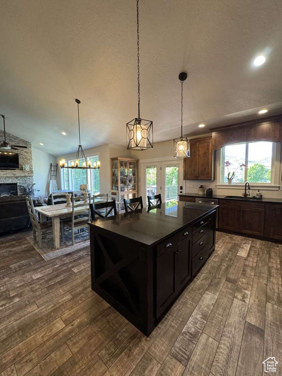 Kitchen with dark wood-type flooring, a stone fireplace, dark countertops, a sink, and recessed lighting