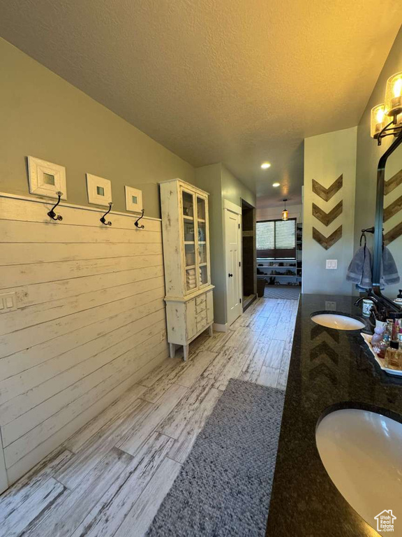 Mudroom with a textured ceiling, light wood finished floors, a sink, and wood walls