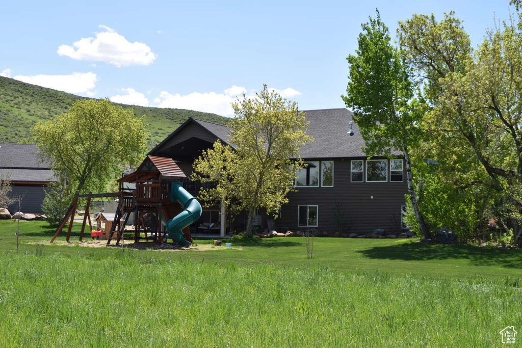 Back of house with a playground, a lawn, and a shingled roof
