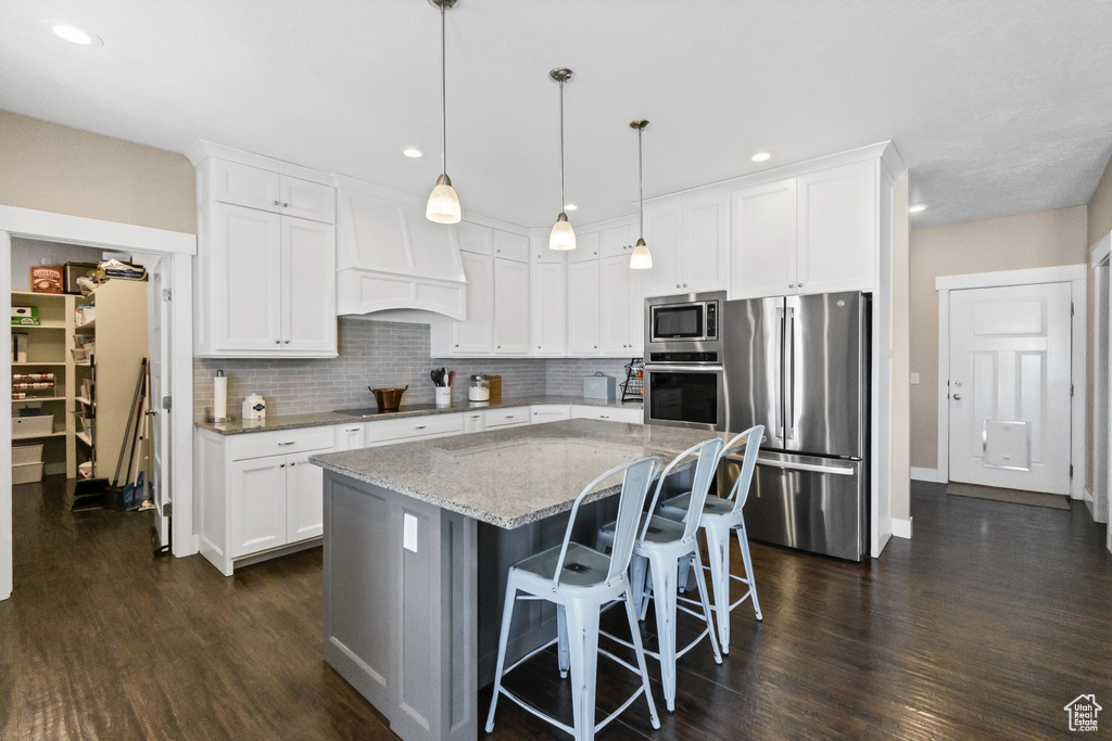 Kitchen with appliances with stainless steel finishes, dark wood-style floors, light stone counters, a center island, and recessed lighting