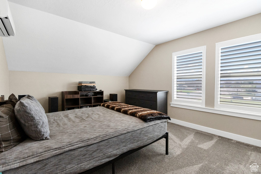Carpeted bedroom featuring a wall mounted air conditioner, baseboards, and lofted ceiling