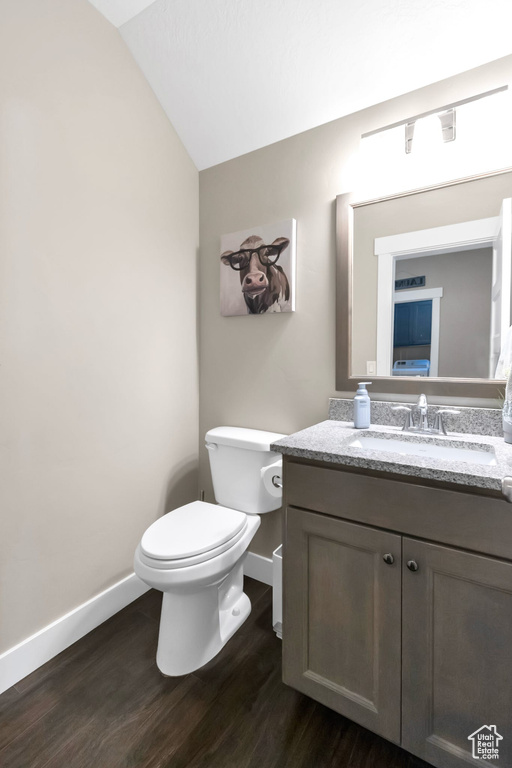 Bathroom featuring baseboards, vanity, wood finished floors, toilet, and vaulted ceiling