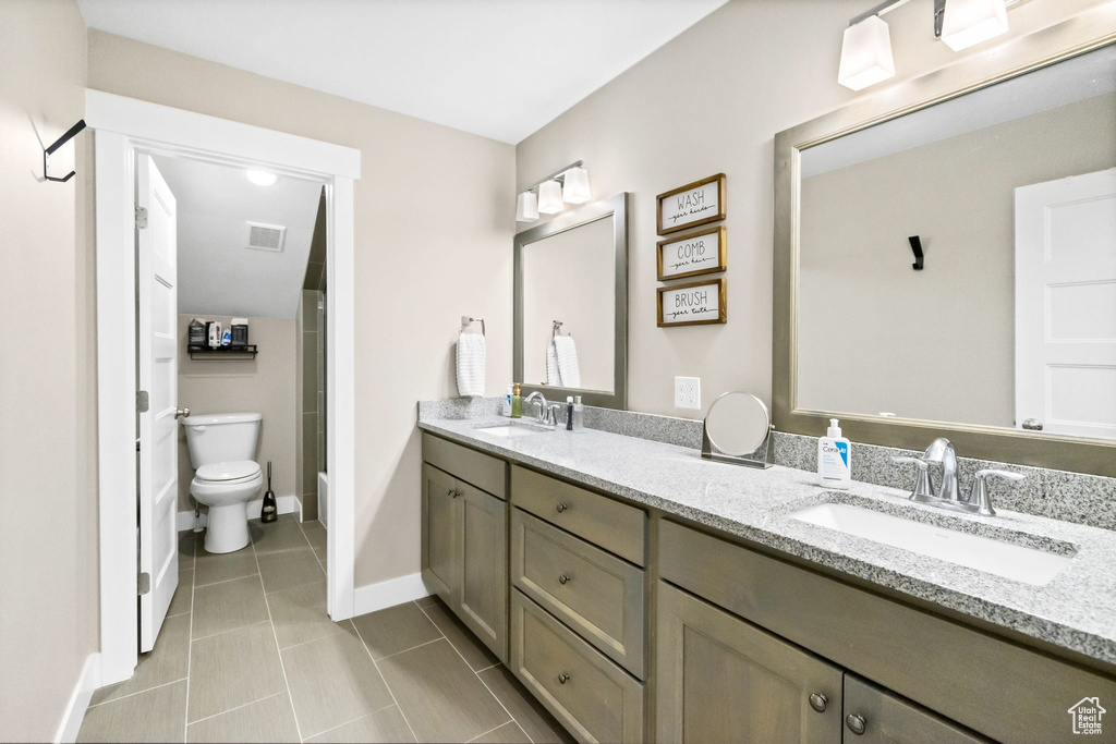 Bathroom featuring double vanity, tile patterned flooring, baseboards, and toilet
