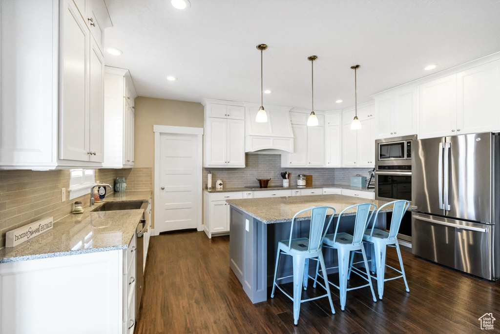 Kitchen with appliances with stainless steel finishes, a sink, a center island, white cabinetry, and recessed lighting