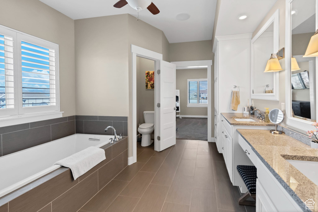 Bathroom with toilet, vanity, ceiling fan, a bath, and baseboards
