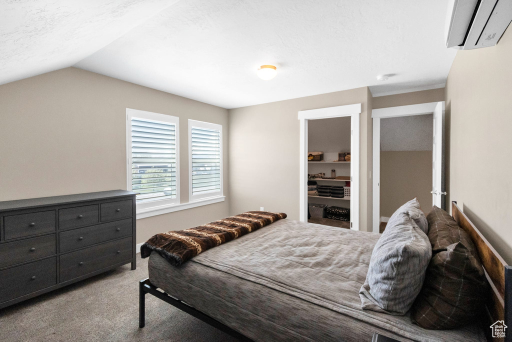 Carpeted bedroom with a wall mounted air conditioner and vaulted ceiling