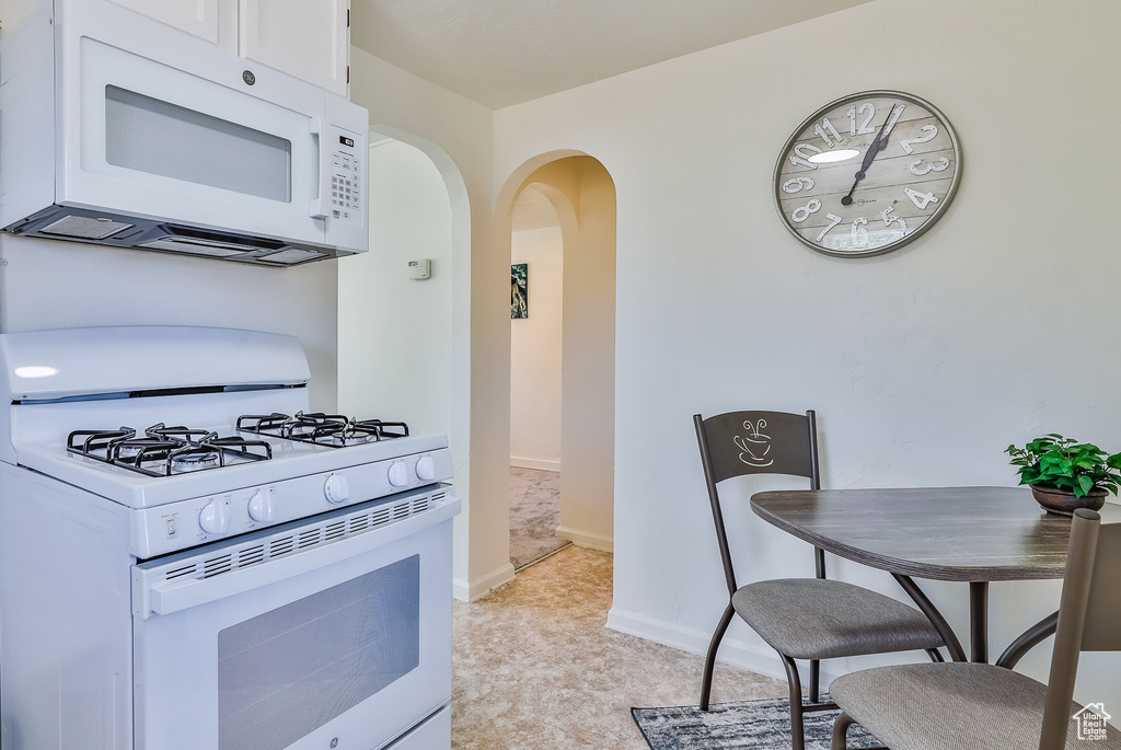 Kitchen with white appliances, arched walkways, white cabinets, baseboards, and light carpet