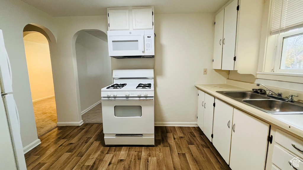 Kitchen featuring white appliances, a sink, dark wood finished floors, white cabinets, and arched walkways