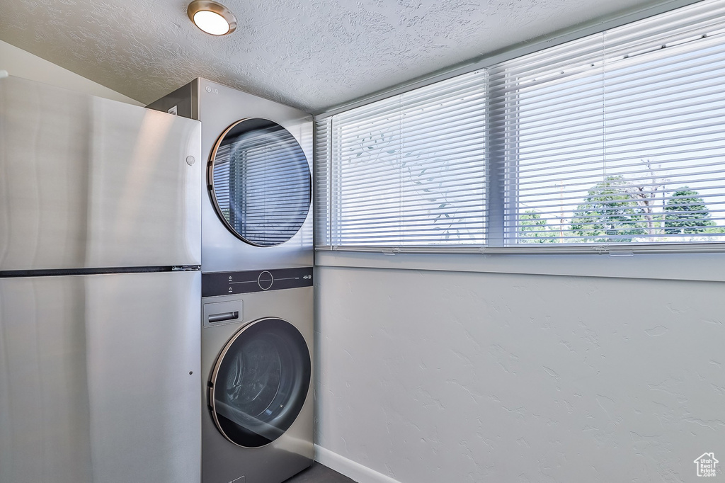 Washroom with stacked washer / drying machine, baseboards, and a textured ceiling