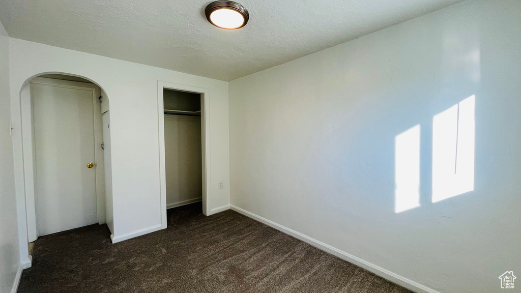 Unfurnished bedroom featuring dark colored carpet, arched walkways, baseboards, and a closet