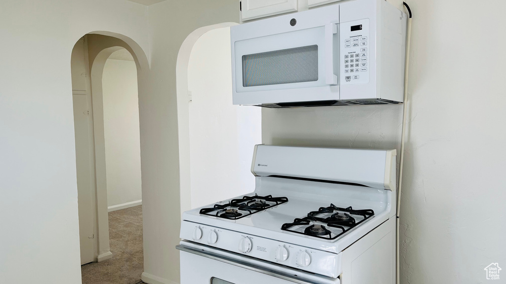 Kitchen featuring white appliances, light colored carpet, white cabinetry, baseboards, and arched walkways