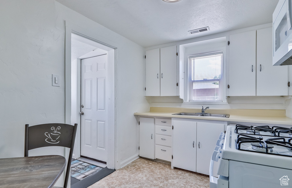 Kitchen with a sink, white appliances, white cabinets, and light countertops