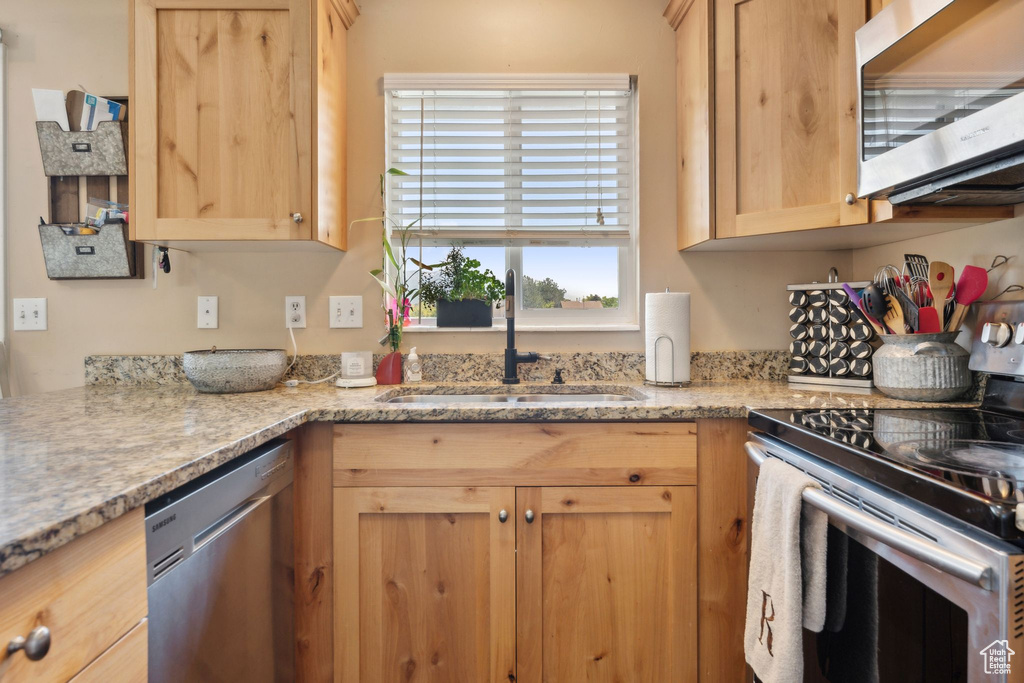 Kitchen with stainless steel appliances, a sink, light brown cabinets, and light stone countertops