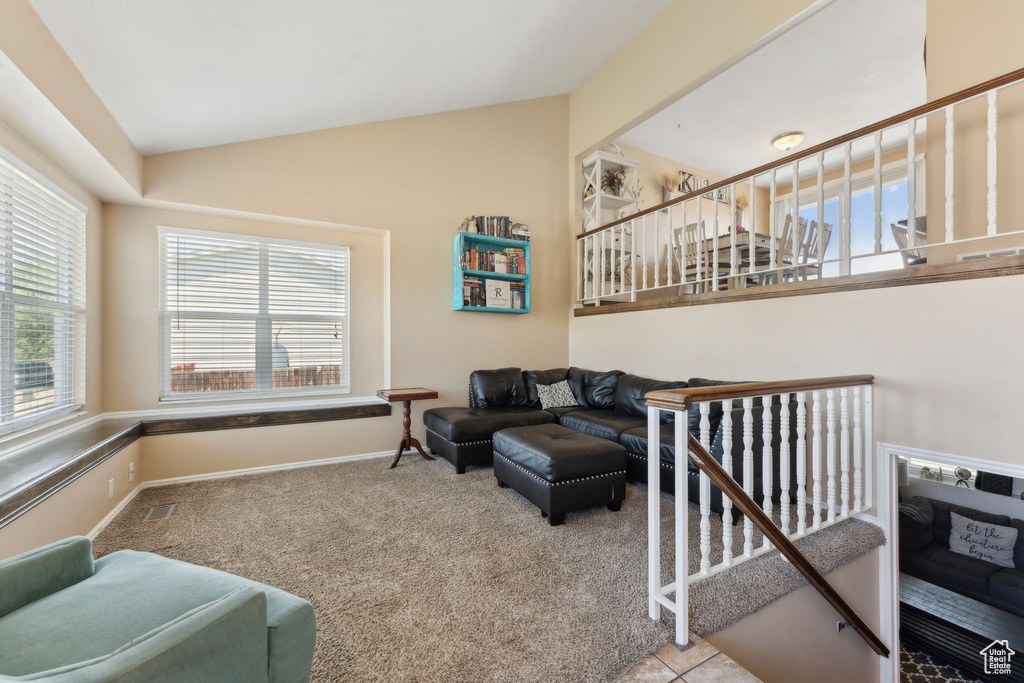 Carpeted living room featuring vaulted ceiling, baseboards, and stairway