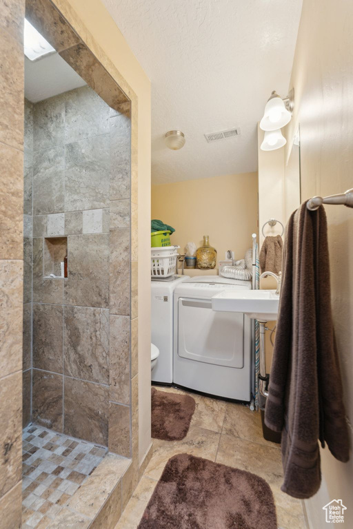 Full bathroom with a tile shower, washing machine and dryer, and toilet