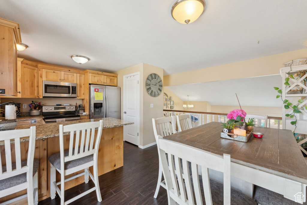 Kitchen featuring appliances with stainless steel finishes, dark wood-style floors, light stone counters, light brown cabinets, and a peninsula