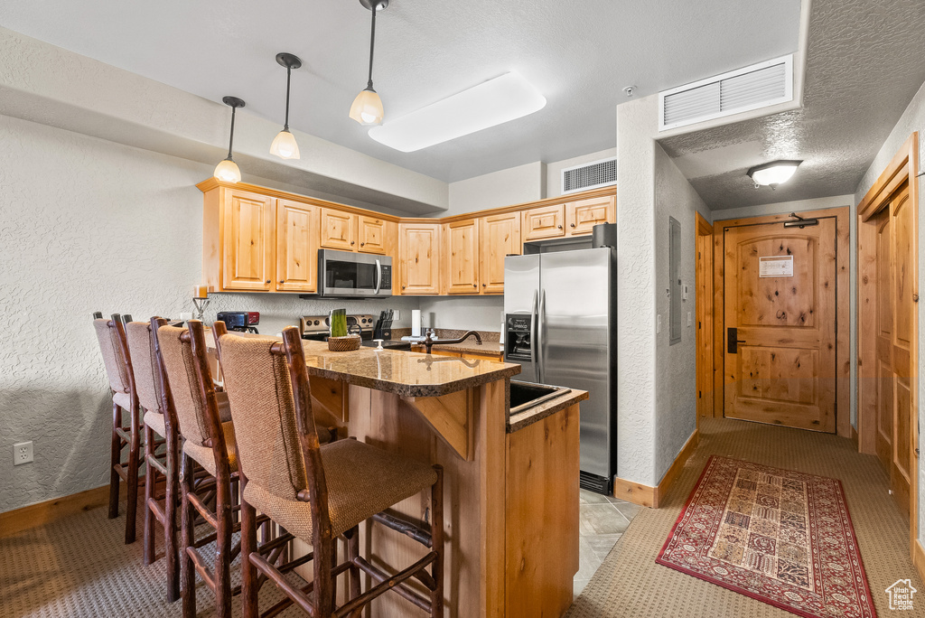 Kitchen with stainless steel appliances, a kitchen bar, dark countertops, a textured wall, and baseboards