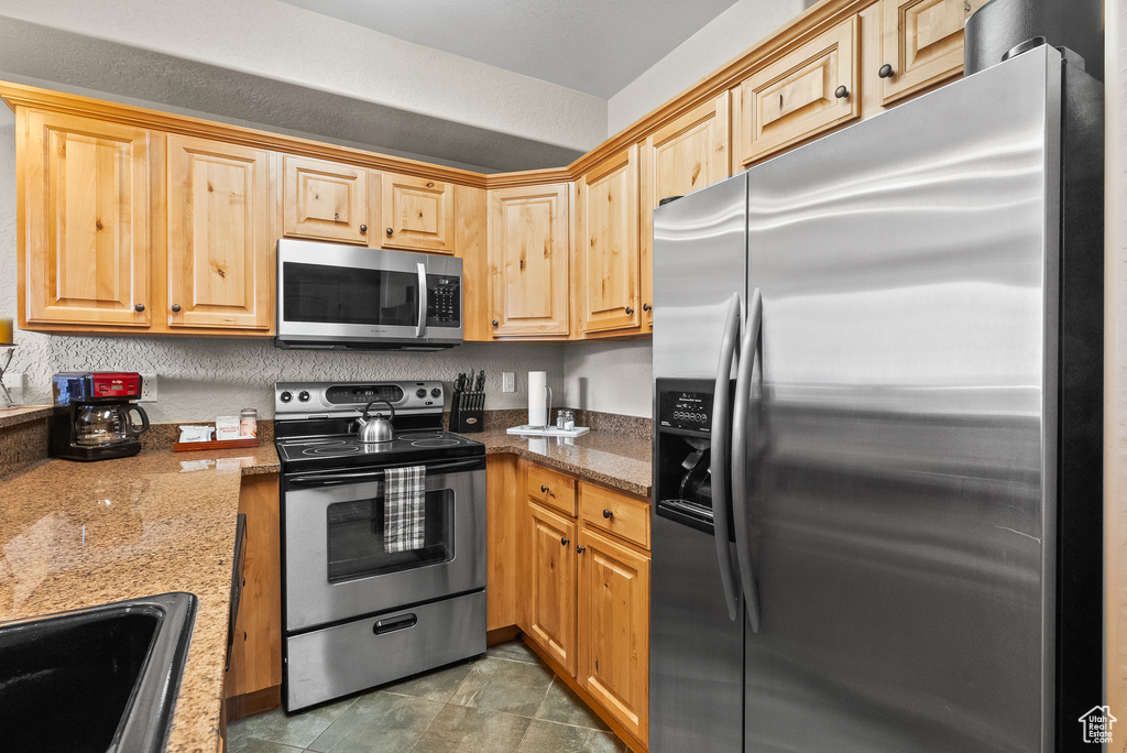 Kitchen with appliances with stainless steel finishes, a sink, and stone countertops