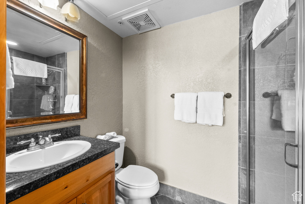 Full bathroom with vanity, a shower stall, toilet, a textured wall, and tile patterned flooring