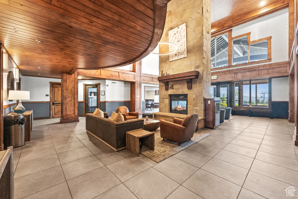 Tiled living area with wooden ceiling, high vaulted ceiling, a wainscoted wall, a fireplace, and wooden walls