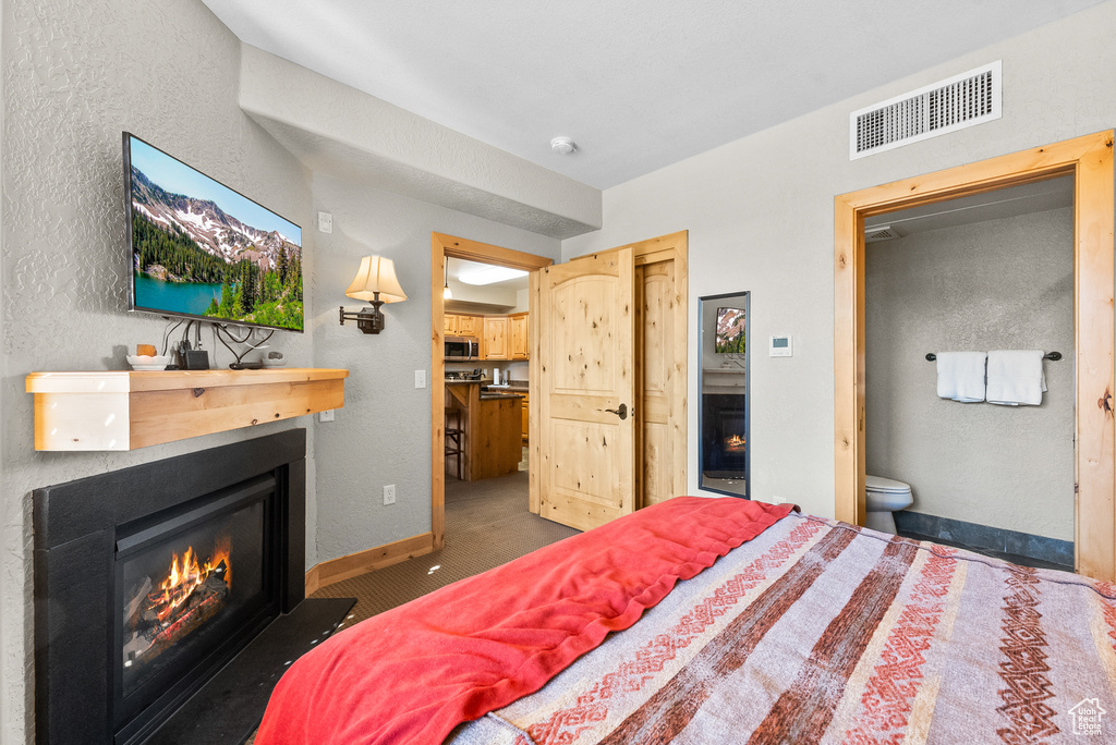Carpeted bedroom featuring a glass covered fireplace, ensuite bathroom, a textured wall, a closet, and baseboards