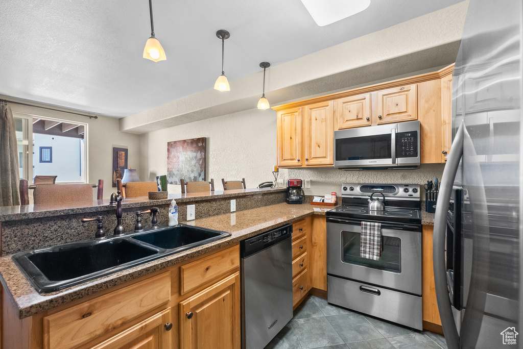 Kitchen with appliances with stainless steel finishes, a sink, a peninsula, pendant lighting, and dark stone countertops
