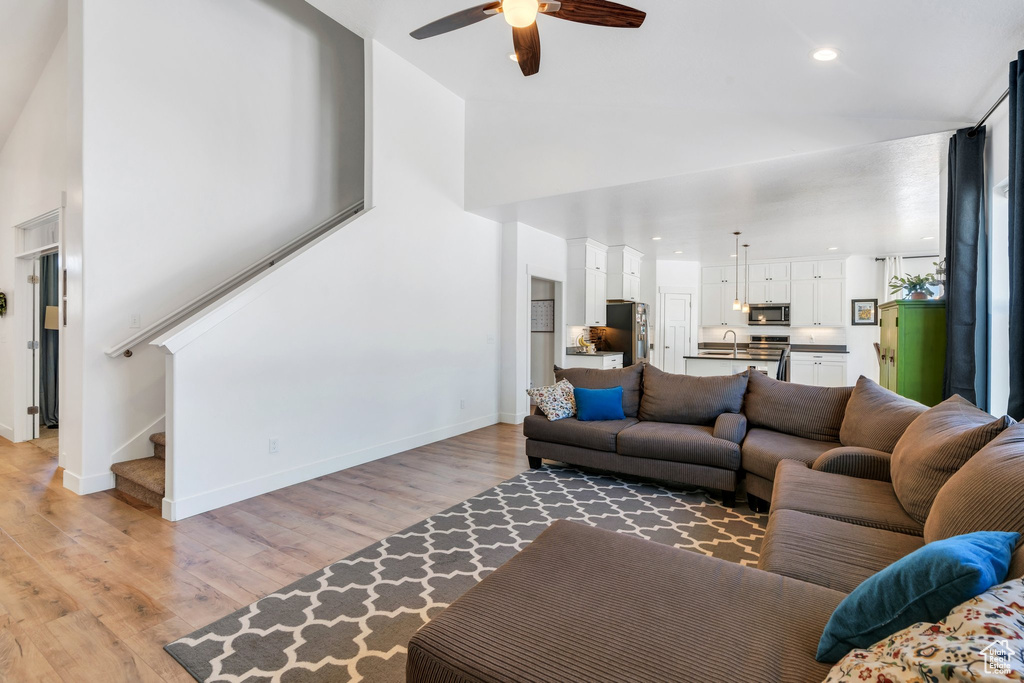 Living room with a ceiling fan, stairs, high vaulted ceiling, light wood-style floors, and baseboards