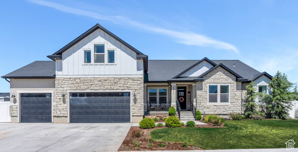 Craftsman-style house featuring board and batten siding, stone siding, a front yard, concrete driveway, and a garage