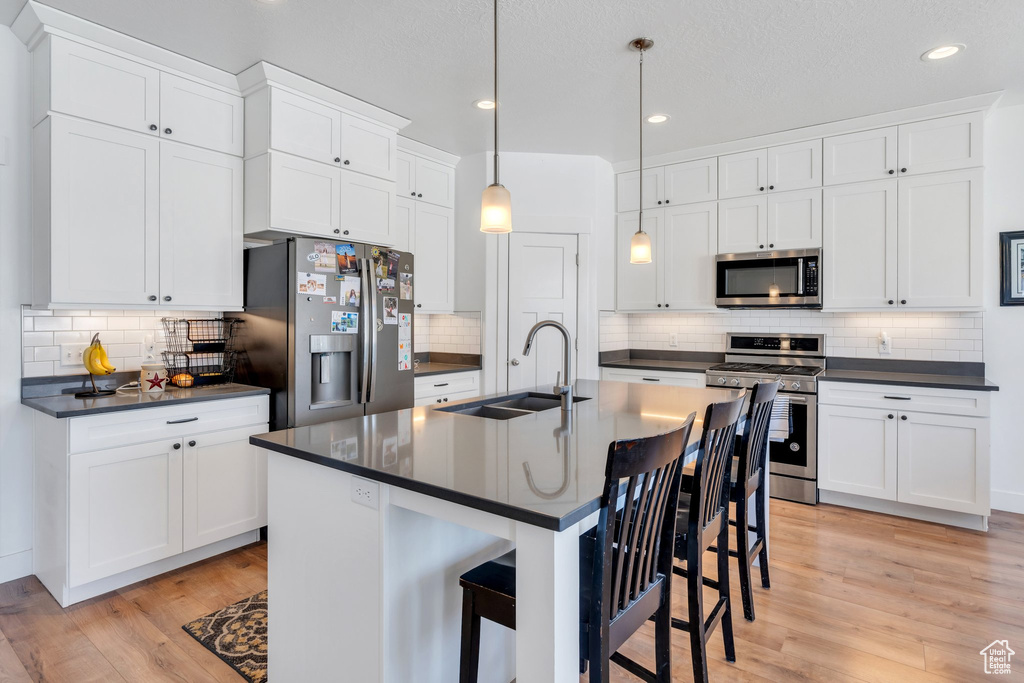 Kitchen with stainless steel appliances, a sink, dark countertops, tasteful backsplash, and white cabinetry
